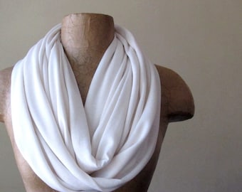 May include: A white infinity scarf made of soft fabric. The scarf is draped over a mannequin's neck and shoulders.