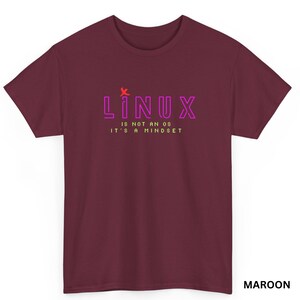 May include: Maroon t-shirt with the text "LINUX" in pink, with a red asterisk above the word, and the text "IS NOT AN OS IT'S A MINDSET" in green. The shirt is a crew neck style.