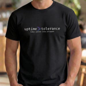 Peut inclure: T-shirt noir avec l'inscription blanche "uptime > tolerance", un symbole de flèche violet et bleu. En dessous, en blanc, "human system limit exceeded". Le t-shirt est à col rond.