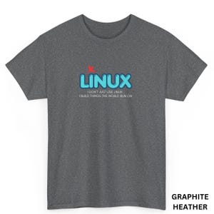 Op de afbeelding: Grafietkleurig heather T-shirt met het woord "LINUX" in blauwe bubbelletters en een rode "X" erboven. De tekst "I DON'T JUST USE LINUX I BUILD THINGS THE WORLD RUN ON" staat onder het woord "LINUX".