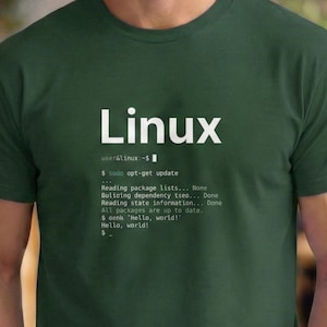 Puede incluir: Camiseta verde oscuro con la palabra "Linux" en letras blancas. Debajo, el texto simula una interfaz de línea de comandos con comandos como "sudo apt-get update" y "Hello, world!"