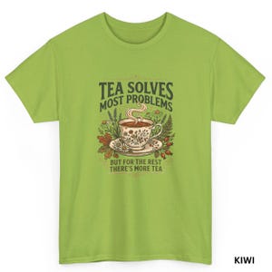 Op de afbeelding: Een kiwi-groen t-shirt met korte mouwen en een centrale afbeelding van een bloemrijke theekop met stoom, omringd door botanische illustraties. De tekst luidt: TEA SOLVES MOST PROBLEMS BUT FOR THE REST THERE'S MORE TEA in donkergroen.