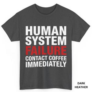 Puede incluir: Camiseta gris oscuro con el texto "HUMAN SYSTEM FAILURE CONTACT COFFEE IMMEDIATELY" en letras blancas y rojas. La camiseta también tiene las palabras "DARK HEATHER" en la esquina inferior derecha.