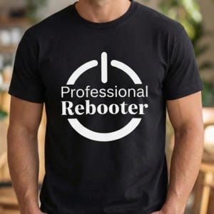 以下が含まれることがあります： 白い電源ボタンのグラフィックと「Professional Rebooter」の文字がプリントされた黒いTシャツ。デザインは太字のサンセリフ体です。Tシャツは柔らかい素材でできており、半袖です。