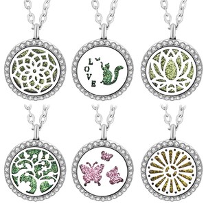Könnte beinhalten: Sechs silberfarbene runde Anhängerketten mit kristallbesetzten Rändern. Die Designs umfassen ein grünes Mandala, eine Katze mit dem Text LOVE, einen grünen Lotus, einen grünen Baum, rosa Schmetterlinge und ein goldenes Sonnenstrahlenmuster.