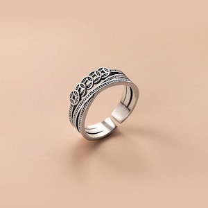 May include: Silver adjustable ring with five coin-shaped decorative elements. The ring has an open design and is set against a soft, neutral background. The ring's design incorporates intricate details and a vintage aesthetic.