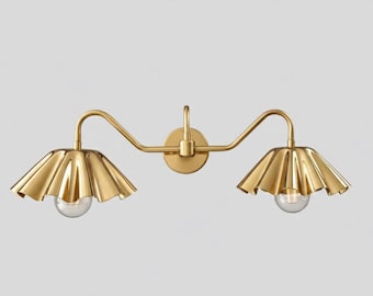 May include: A gold-colored, two-light vanity fixture. The fixture features two ruffled, petal-shaped shades and clear glass bulbs. The fixture is mounted on a round backplate and has a curved arm design.