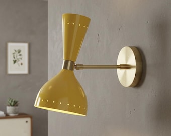 May include: A wall-mounted lamp featuring a dual-cone yellow metal shade with small perforated holes along the edges. The fixture includes a brass-toned horizontal arm and a circular wall plate, providing a focused light source for interior spaces.