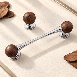 May include: A cabinet handle and a matching knob featuring spherical dark brown wood ends with a polished silver metal center. The handle and knob both display the engraved letters SHN on the silver metal components, with the handle featuring a tapered design.