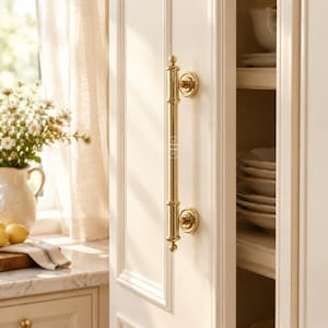 Peut inclure: Une poignée de placard en laiton poli au design cylindrique, dotée de deux bases de montage circulaires et d'embouts décoratifs en haut et en bas, installée verticalement sur une porte de placard blanche avec un logo gravé visible.