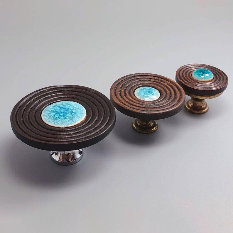 May include: Three decorative cabinet knobs with a dark brown, grooved design. Each knob features a circular, light blue center. The knobs have different base finishes: silver, brass, and gold.