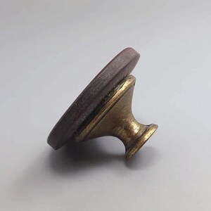 May include: A seal stamp with a round, dark brown surface and a decorative, antique brass-colored handle. The stamp is angled, showcasing its design and the handle's details. Ideal for crafts and stationery.