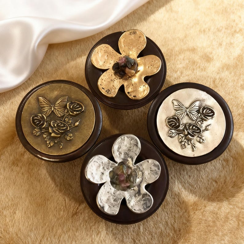 May include: Four decorative cabinet knobs with dark brown bases. Two knobs feature butterfly and rose designs, while the other two have flower designs. The metal accents are in gold and silver tones, adding a touch of elegance.
