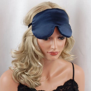 May include: A navy blue satin sleep mask with a black elastic band. The eye mask is worn by a mannequin with blonde hair and a black lace-trimmed top. The mask is designed to block out light for better sleep.