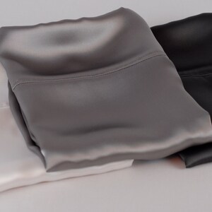 May include: Three satin pillowcases in white, gray, and black. The pillowcases are folded and stacked on top of each other.