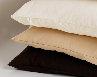 May include: Three pillows stacked on top of each other. The top pillow is white, the middle pillow is beige, and the bottom pillow is brown.