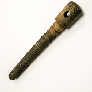 May include: A wooden screw with a threaded shaft and a cylindrical head. The head has a hole drilled through it. The screw is made of aged wood and is set against a white background.
