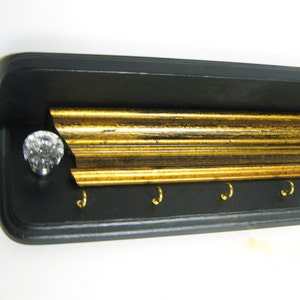 May include: Black key holder with a gold trim and five hooks. The key holder has a crystal knob.