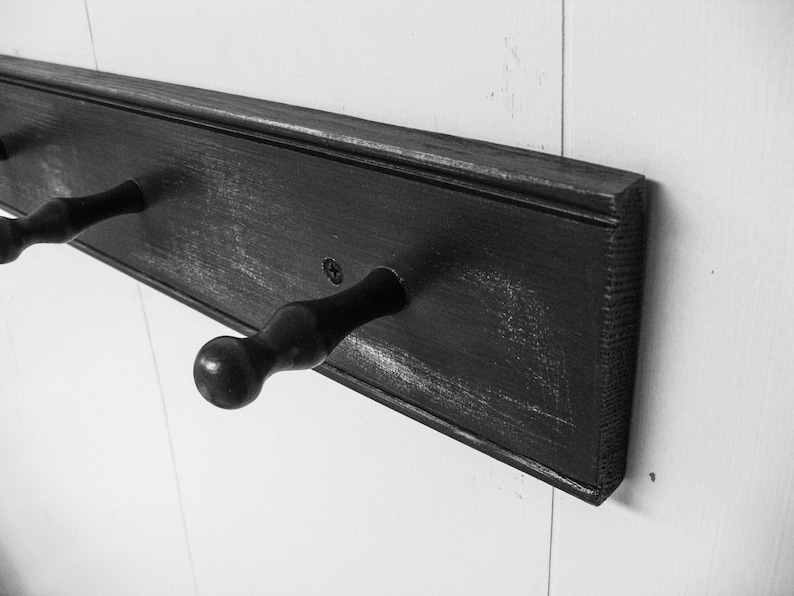 May include: A black wooden coat rack with three hooks. The rack is mounted on a white wall.