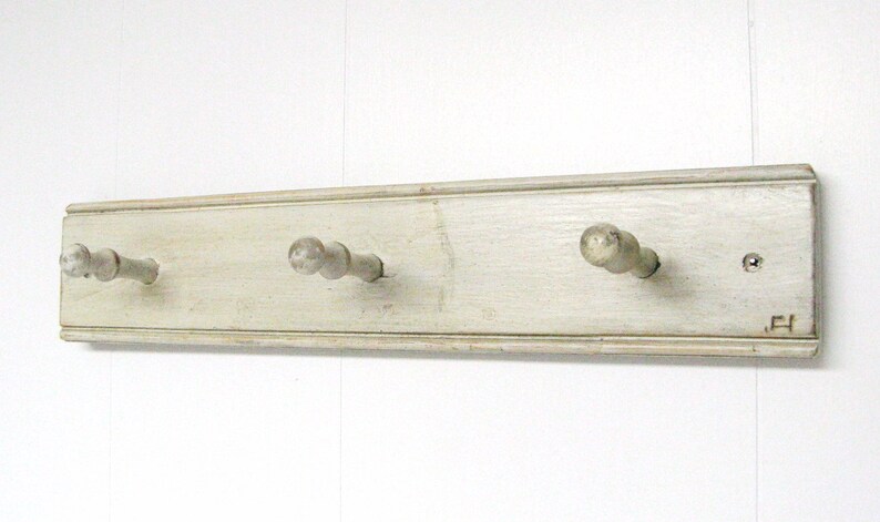 May include: White wooden wall mounted coat rack with three knobs. The rack has a distressed finish and the knobs are painted a light gray.