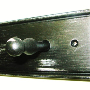 May include: Black wooden wall mounted coat rack with a single black knob hook. The wood has a distressed finish.