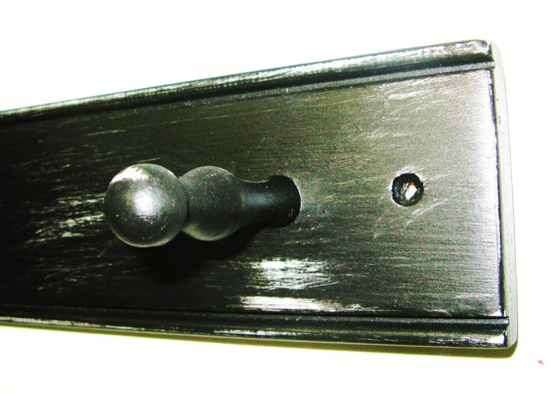 May include: Black wooden wall mounted coat rack with a single black knob hook. The wood has a distressed finish.