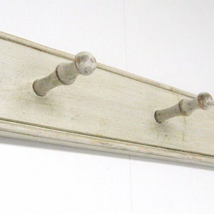 May include: White wooden wall mounted coat rack with three hooks. The hooks are made of wood and have a rounded knob at the end.
