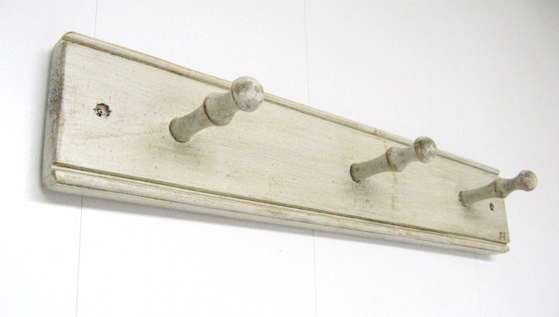 May include: White wooden wall mounted coat rack with three hooks. The hooks are made of wood and have a rounded knob at the end.
