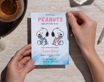 May include: A baby shower invitation featuring two cartoon Snoopy characters, one in blue and one in pink, with pacifiers. The text reads "A Little Peanuts Are On The Way!" and includes event details. The invitation is held by two hands.