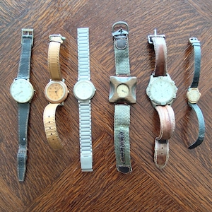 Puede incluir: Una colección de relojes de pulsera con varios estilos de correas, incluyendo cuero, metal y tela. Las esferas de los relojes son redondas, con diferentes colores y diseños. Los relojes se exhiben sobre una superficie de madera.