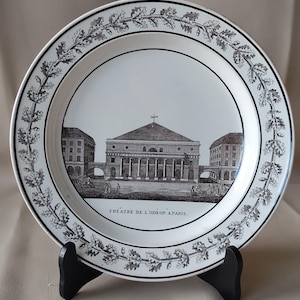 May include: A white ceramic plate with a black and white illustration of a building, likely a theater, and the text "THEATRE DE L'ODEON A PARIS." The plate has a decorative border of leaves and is displayed on a black stand.