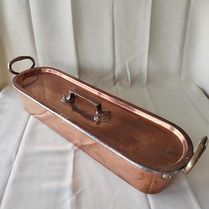 Pode incluir: Uma caneca de cerâmica branca com uma alça preta e o texto "But First, Coffee" em negrito preto. A caneca está sobre um fundo desfocado, sugerindo um ambiente acolhedor.