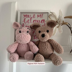 Könnte beinhalten: Zwei handgefertigte gehäkelte Stofftiere: ein rosa Nilpferd und ein hellbrauner Bär. Das Nilpferd hat schwarze Augen und der Bär hat eine schwarze Nase. Der Hintergrund enthält einen gerahmten Druck mit dem Text "YOU & ME belong to each other".