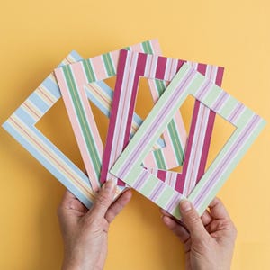 May include: A collection of colorful striped picture mats in various pastel shades, including blue, pink, green, and purple. The mats are held against a yellow background, showcasing their rectangular cut-out design.