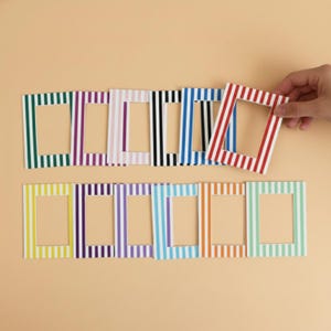 May include: A selection of striped picture frames in a range of colours, including green, purple, white, black, blue, red, yellow, and orange. One frame is held by a hand. The frames are rectangular with a central aperture.