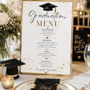 May include: A graduation menu with a gold frame, featuring appetizers, entrées, sides, and desserts. The menu includes a graduation cap graphic and the words "Graduation MENU." A small graduation cap and a candle are on the table.
