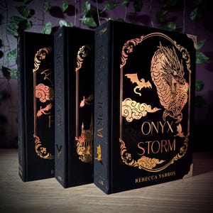 May include: Three hardcover books with black covers and gold foil accents. The book spines read "ONYX STORM". The covers feature gold illustrations of a dragon, clouds, bats, and other decorative elements. The author's name, Rebecca Yarros, is printed on the front cover.
