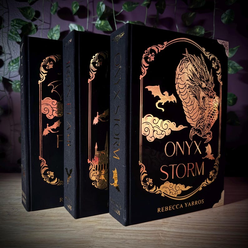 May include: Three hardcover books with black covers and gold foil accents. The book spines read "ONYX STORM". The covers feature gold illustrations of a dragon, clouds, bats, and other decorative elements. The author's name, Rebecca Yarros, is printed on the front cover.