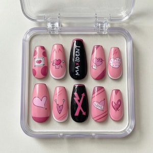 Puede incluir: Un juego de diez uñas postizas rosas con varios diseños de corazones y el texto "MAX|DENT" en una uña. Las uñas están en una caja de plástico transparente. Los diseños incluyen corazones, amor y otros patrones.