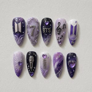 May include: A set of ten artificial nails with a purple and white color scheme. Each nail features unique designs, including the number 7, musical notes, the letters "BTS" and "ARMY", and various heart and star accents.