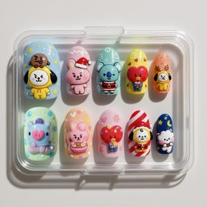 May include: A set of ten artificial nails with cartoon character designs. The nails are in a clear plastic case. Each nail features a different character in various colors, including blue, pink, yellow, and orange. The designs include a bunny, koala, and other characters.