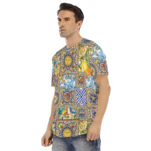Peut inclure: Un t-shirt à manches courtes avec un motif coloré. Le motif présente une mosaïque de carrés avec des soleils, des citrons et des motifs floraux dans des tons de bleu, jaune et rouge. Le t-shirt est porté par une personne.
