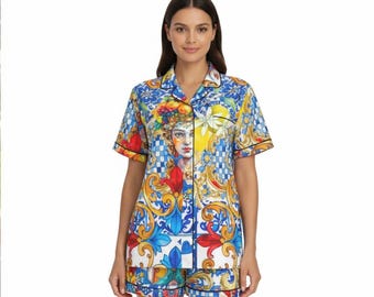 May include: A patterned pajama set with a short-sleeved shirt and shorts. The design features a portrait of a woman, floral motifs, and geometric shapes in blue, yellow, and red, with black trim.