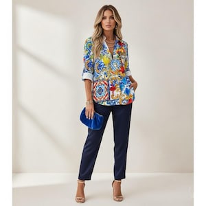 May include: A button-down shirt with a colorful floral and tile pattern, paired with navy blue pants and gold heels. A blue clutch is held in the hand. The shirt has rolled-up sleeves.