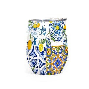 May include: A stemless wine tumbler with a decorative patchwork design. The design features lemons, blue floral patterns, and geometric tiles in yellow, blue, and white. The tumbler has a silver-colored lid.