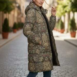 May include: A long, hooded puffer coat with a floral pattern in shades of brown, green, and red. The coat is worn over a black top and blue jeans. The coat has a zip closure and pockets.