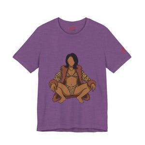 Può includere: T-shirt viola con un'illustrazione di una persona con un bikini leopardato e un cappotto di pelliccia marrone. L'illustrazione è centrata sulla maglietta. La maglietta ha un piccolo logo in alto a sinistra e sulla manica destra.