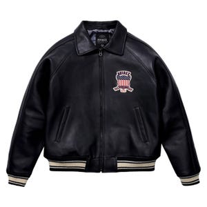 May include: Black leather jacket with a collared neckline and a zip-up front. The jacket features a patch on the chest with the text "AVIREX" and an American flag design. The cuffs and hem have a cream and black striped pattern.