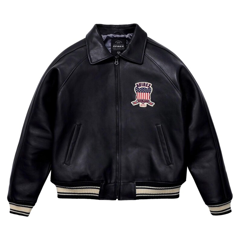May include: Black leather jacket with a collared neckline and a zip-up front. The jacket features a patch on the chest with the text "AVIREX" and an American flag design. The cuffs and hem have a cream and black striped pattern.