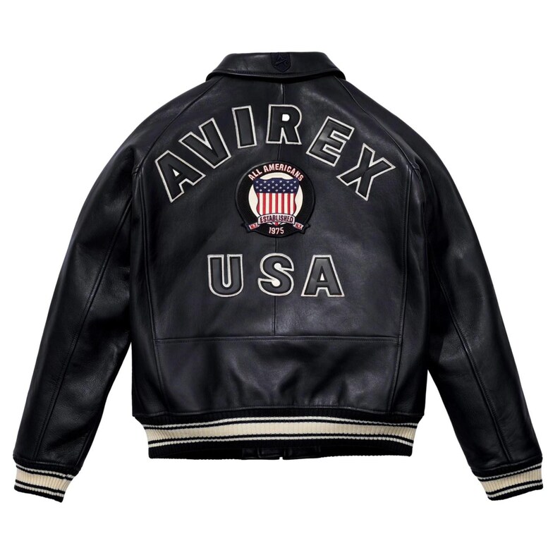 May include: Black leather jacket with the word "AVIREX" arched across the shoulders in white lettering. Below the word "AVIREX" is a patch with the American flag and the words "ALL AMERICANS ESTABLISHED 1975". The word "USA" is below the patch.